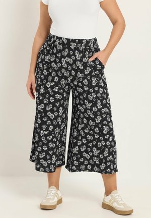 Sorte, vide bukser med korte ben og hvidt tusindfrydmønster, elastisk talje, sidelommer, båret med hvid top og beige sneakers.