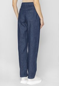 Ciemnoniebieskie dżinsowe spodnie typu straight-leg z wysokim stanem, dwoma tylnymi kieszeniami i czystym przeszyciem. W połączeniu z białymi sneakersami.