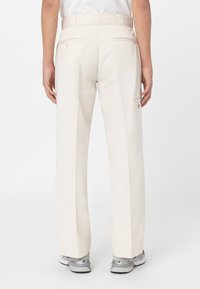 Pantalones de color beige claro, confeccionados en tejido suave, con un diseño de pierna recta, dos bolsillos traseros y un discreto detalle de logo en el lateral.