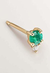 Pendiente de oro que presenta una gran gema verde redonda y una piedra clara más pequeña, montadas en un engaste de garras con un acabado liso y brillante.