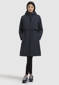 Manteau imperméable bleu marine foncé avec fermeture éclair à l'avant, capuche et poches. Conçu en tissu lisse avec un design à demi-superposition.