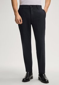 Marineblauwe op maat gemaakte broek van een gestructureerde stof, met zijzakken en een knoopsluiting, gecombineerd met zwarte leren schoenen.