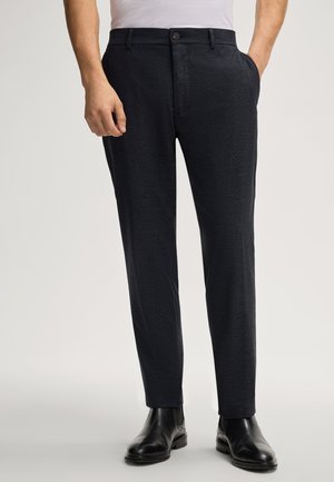 Marineblauwe op maat gemaakte broek van een gestructureerde stof, met zijzakken en een knoopsluiting, gecombineerd met zwarte leren schoenen.