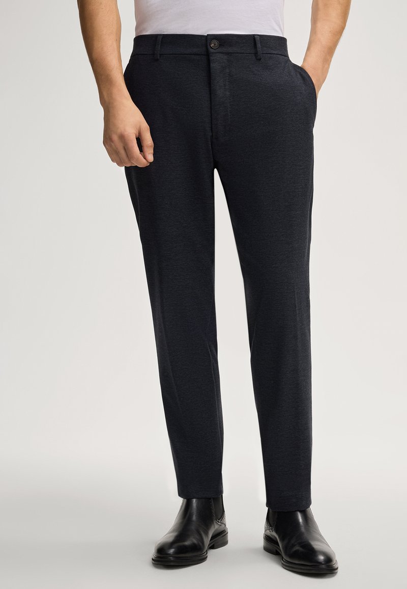 Marineblauwe op maat gemaakte broek van een gestructureerde stof, met zijzakken en een knoopsluiting, gecombineerd met zwarte leren schoenen.