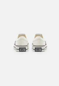 Płócienne trampki w odcieniu off-white z czarnymi akcentami, wyposażone w czarną gumową podeszwę, klasyczny okrągły czubek i charakterystyczne logo All Star na pięcie.