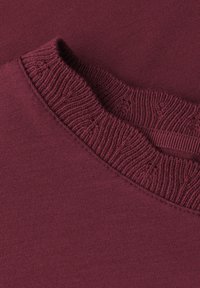 Gros plan d'un pull tricoté bordeaux plié montrant un col rond côtelé et une texture de tissu tricoté lisse.