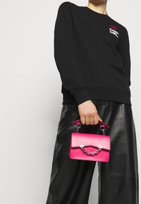 Czarna bluza z haftowanym napisem, w połączeniu z małą, usztywnioną torebką w kolorze intensywnego różu z metalowym łańcuszkiem i górnym uchwytem.