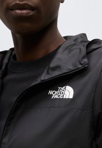 Prikaz izbliza osobe u crnoj The North Face jakni sa djelomično zatvorenim patentnim zatvaračem sprijeda i vidljivim logotipom na prsima.
