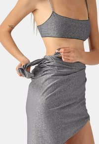 Completo metallico grigio composto da due pezzi con top corto aderente e gonna avvolgente. Il tessuto ha una superficie lucida e brillantinata, che mette in evidenza un design elegante.