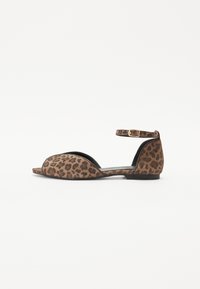 Leopard print flat sandal with open toe design, ankle strap, brown suede material, and a low black sole. Detailed stitching on edges.
