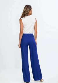Biała bezrękawnik zestawiona z wysokimi, szerokimi spodniami w królewskim niebieskim kolorze. Gładki materiał, dopasowany krój, subtelne detale tylnej kieszeni.