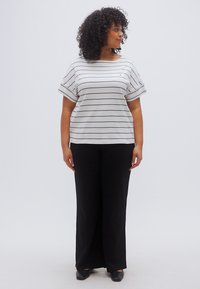 Ριγέ γκρι και λευκό κοντομάνικο τοπ συνδυασμένο με μαύρο παντελόνι φαρδιάς γραμμής· το τοπ έχει άνετη εφαρμογή και στρογγυλή λαιμόκοψη.