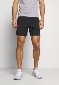 Bermudas deportivas negras con una textura suave, cuentan con bolsillos laterales y un logo reflectante de Nike. Combinadas con zapatillas deportivas blancas.