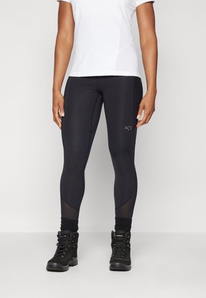 Sorte atletiske leggings med mesh-paneler, parret med en hvid t-shirt med korte ærmer og sorte vandresko med strukturerede snørebånd.