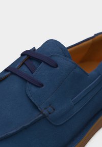 Κοντινό πλάνο μπλε σουέντ παπουτσιού με ναυτικό κορδόνι, λεπτομερείς ραφές και καφέ εσωτερική επένδυση.