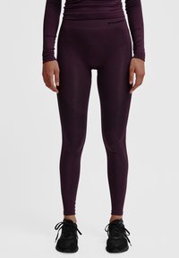 Leggings viola scuro realizzati in un tessuto elasticizzato, con una vita alta e dettagli testurizzati lungo i lati. Scarpe da ginnastica nere completano il look.
