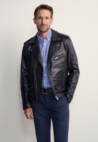 Czarna skórzana kurtka motocyklowa z asymetrycznym zamkiem błyskawicznym, kołnierzem na zatrzask i dwoma przednimi kieszeniami; nałożona na niebieską, w kratę koszulę.