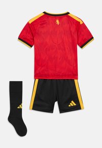 Κόκκινη φανέλα ποδοσφαίρου με κίτρινες και μαύρες λεπτομέρειες, μαύρο σορτσάκι με κίτρινες ρίγες και μαύρη κάλτσα με κίτρινο λογότυπο, απλωμένα επίπεδα.