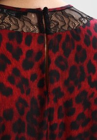 Rød og sort leopardmønster kjole med et blondertrim ved halsudskæringen og en nøglehulåbning på ryggen, forsynet med to sorte knapper.