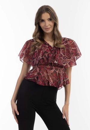 Peplum-Bluse mit rotem und schwarzem Schlangenmuster, transparenten kurzen Ärmeln und Schleife am Ausschnitt, kombiniert mit schwarzen, figurbetonten Hosen.