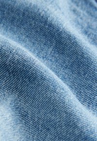 Denimová tkanina v světle modré barvě se soft texturou. Viditelný křížový vzor tkaní, mírně zmačkaný a přeložený. Hladký povrch.