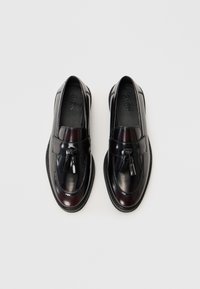 Mocasines de cuero negro con acentos de borlas, superficie lisa, puntera redondeada y detalles de costura en contraste. Suela plana para un uso fácil.