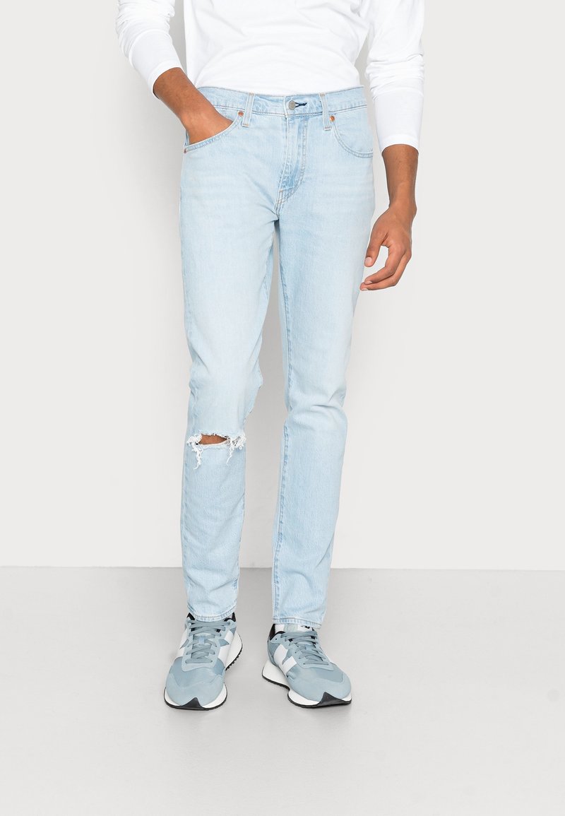 Jasnoniebieskie dżinsy o slim fit z wyrwanym detalem na kolanie. W połączeniu z szarymi butami sportowymi o teksturowanym wzorze.