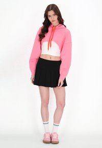 Sudadera corta rosa con cordones naranjas, falda plisada negra, zapatillas rosas y calcetines blancos con rayas verdes. Diseño sencillo y look casual.