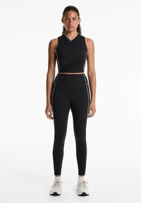 Black athletic outfit featuring a sleeveless crop top with white accents and high-waisted leggings, made from stretchy fabric.