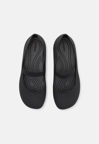 Scarpe Crocs nere con una superficie liscia, forma arrotondata e suola piatta. Presentano una fibbia elastica nera sul collo del piede.