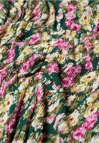 Stof met een bloemenpatroon met roze en gele bloemen op een groene achtergrond. Het materiaal heeft een gekreukte textuur met geplooide details.