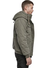 Olivgrüne Kapuzenjacke mit Reißverschluss vorne, zwei Seitentaschen und gerippten Bündchen. Aus einem strukturierten, strapazierfähigen Material gefertigt.
