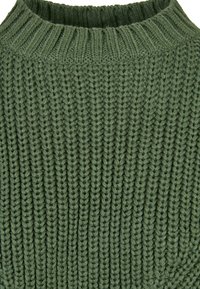 Pull vert en maille avec une texture côtelée et un col haut et arrondi. Le fil est épais, ce qui lui confère un aspect chaleureux.