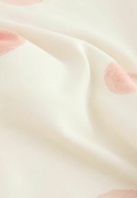 Mäkká biela látka s jemnými ružovými bodkami, zobrazujúca jemné záhyby a hladkú pletenú štruktúru.