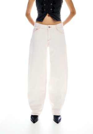 Persona che indossa pantaloni bianchi a vita alta e gamba larga, scarpe nere con punta e top corto senza maniche nero con bottoni decorativi.