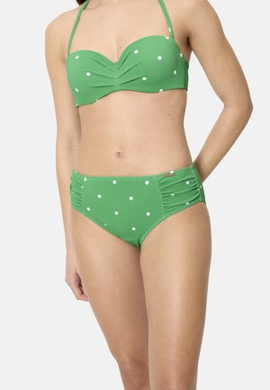 Mujer que lleva un bikini verde con lunares blancos, que consta de un top halter y braguitas de talle alto con frunces.