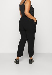 Zwarte joggerbroeken met een taps toelopend ontwerp, voorzien van zijzakken en een contrasterende witte strook langs de zijkanten, gecombineerd met een zwart tanktop.