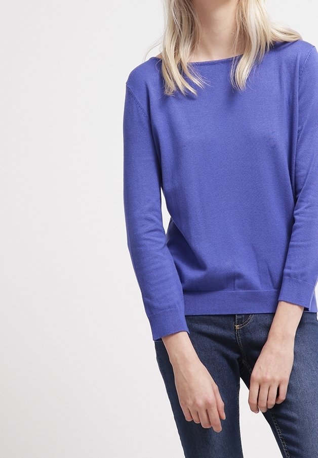 Intensywnie fioletowy sweter z dzianiny z okrągłym dekoltem i długimi rękawami, z prążkowanymi mankietami i dołem. Połączony z ciemnoniebieskimi dżinsami.