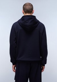 Felpa con cappuccio blu navy caratterizzata da una vestibilità ampia, una texture morbida e polsini a coste. Dettagli delle cuciture su spalle e schiena.