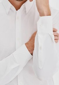 Biała koszula zapinana na guziki z długimi rękawami; gładki, lekki materiał; posiada klasyczny kołnierzyk i zaokrąglone mankiety z zapięciem na pojedynczy guzik.