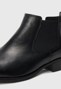 Bottines en cuir noir avec des panneaux latéraux élastiques, bout rond et petit talon empilé. Texture lisse et détails de couture minimaux.