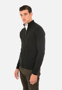 Cardigan nero con zip, dotato di collo alto, polsini a coste e dettagli con zip, realizzato in un tessuto a maglia liscia.
