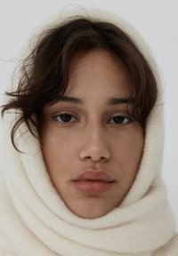 Kremowy wełniany szal owinięty wokół głowy, prezentuj�ący miękką, teksturowaną powierzchnię. Neutralne tło podkreśla szczegóły szala.