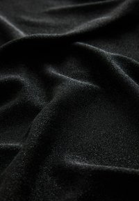 Fekete szövet sima textúrával, amely finom fényességet és lágy redőket mutat, kiemelve könnyű és puha összetételét.