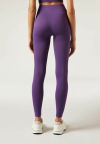 Hoge paarse legging met ribbelstructuur, nauwsluitend ontwerp, zachte elastieken tailleband, en gecombineerd met witte sportschoenen.