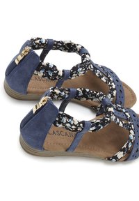 Blaue, perforierte Sandalen mit Stoffriemen im Blumenmuster und einem goldenen Reißverschluss-Detail. Flache Sohle und gepolsterter Innenraum.