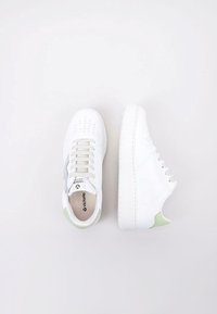 Baskets blanches avec un dessus en cuir lisse. Présentent un accent vert clair sur le talon et un panneau latéral gris. Zone des orteils légèrement perforée.