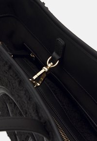 Svart handväska inuti med en slät läderfoder, en mjuk textilstruktur, guldfärgad dragkedja och en minimalistisk design.