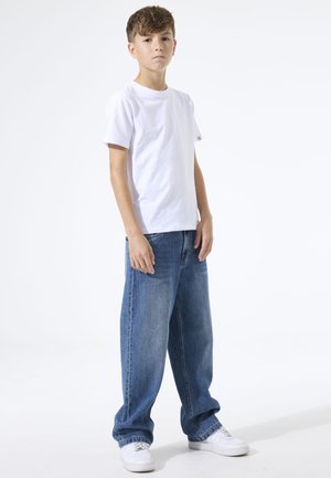 T-shirt en coton blanc à manches courtes, associé à un jean denim bleu ample. Des baskets blanches complètent cette tenue décontractée.