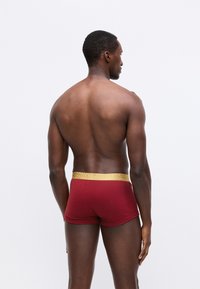 Röda boxershorts med ett strukturerat guldmidjeband. Materialet verkar mjukt och åtsittande, vilket framhäver en enkel, enhetlig design.